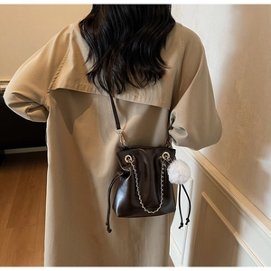 Detail of a dark brown drawstring bucket bag with silver chain and white pom pom charm