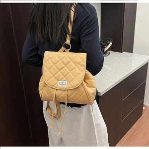 Detail view of quilted camel backpack featuring a silver metal twist lock and drawstring