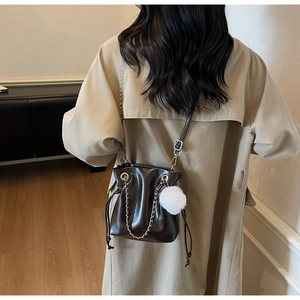 Detail of dark brown bucket bag with shiny leather texture and decorative white fur pompom