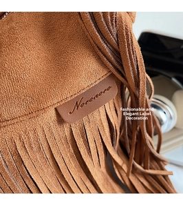 Macro shot of brown suede tassel handbag showing leather brand patch and fine texture
