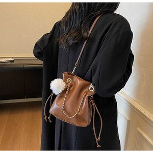 Sac seau en cuir marron avec chaîne dorée et charmant pompon blanc moelleux en détail