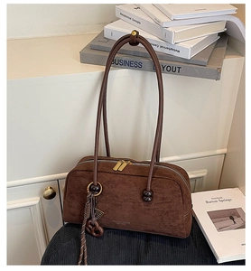 Detailed view of a brown suede underarm bag with gold zippers and decorative cord charms.