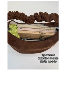 Draufsicht auf das geräumige Innere einer braunen Wildledertasche mit Handy und Büchern