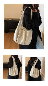 Detail view of cream shoulder bag featuring multiple functional pleated pockets and wide strap