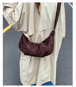 Close-up of a minimalist dark brown suede half-moon crossbody bag in high fashion street style