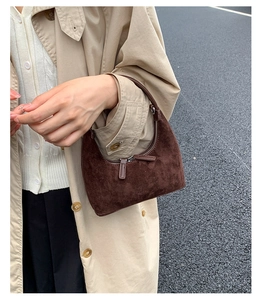 Close-up of retro brown suede hobo bag with zipper and matte texture on a street background
