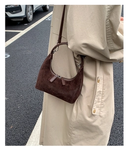 Detail of dark brown suede crescent bag worn with a beige trench coat in a street style look