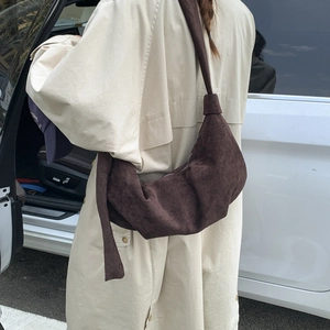 Detail of dark brown suede crescent bag with knot shoulder strap on beige trench coat