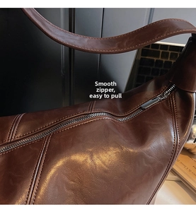 Detail view of smooth silver metal zipper on dark brown textured leather shoulder bag