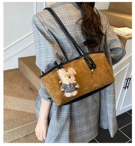 Sac cabas en daim marron avec anses noires et charm ours en peluche porté par le modèle