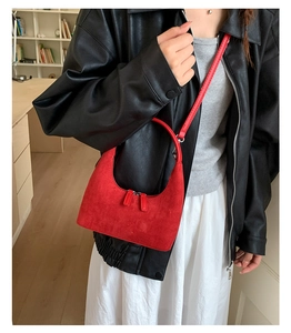 Close-up of a red suede crescent hobo bag with sleek metal zippers and slim shoulder strap
