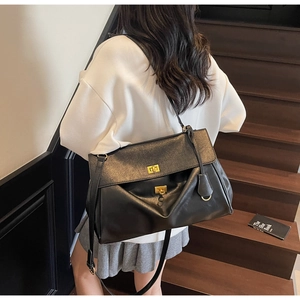 Detail of a large matte black tote bag with dual gold twist locks on an urban shoulder strap