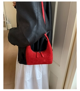 Detail view of red suede shoulder bag with dual zipper closure and slim strap on model