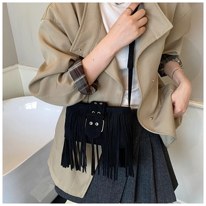 Détail du sac à franges en daim noir avec œillets métalliques porté avec un trench beige
