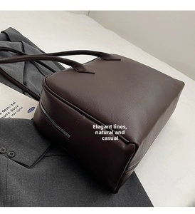 Dettaglio della borsa tote in pelle marrone scuro con cerniera metallica su sfondo grigio