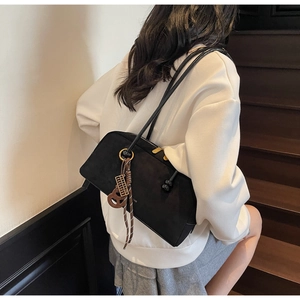 Detail of black matte shoulder bag with vintage tassel and metal abacus charm on model