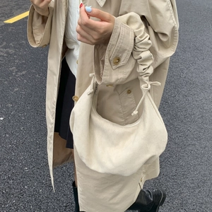 Detail of beige suede crescent bag with ruched handle and drawstring on a trench coat