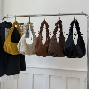 Close-up of ruched hobo bags in various suede colors hanging on a metal rack