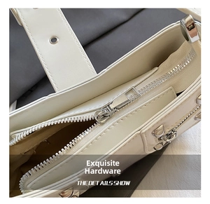 Detail showing high-quality silver metal zipper and buckle on a cream underarm bag