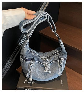 Close-up of vintage washed denim crescent bag featuring multiple zippers and fringe detail