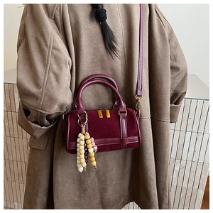 Detail of burgundy suede boston bag with round beads charm and golden metal zipper