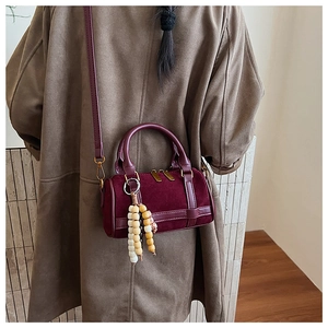 Detail of burgundy mini Boston bag with suede texture and wooden bead tassel accessory