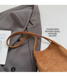 Detailed close-up of brown suede shoulder bag featuring slim straps and beige stitching