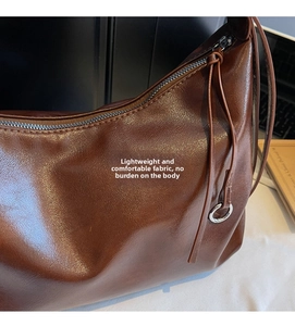 Close-up detail of soft dark brown leather texture and silver ring zipper on tote bag
