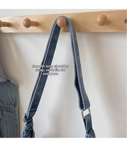 Detail of adjustable denim shoulder strap with silver metal buckle on a wood hook