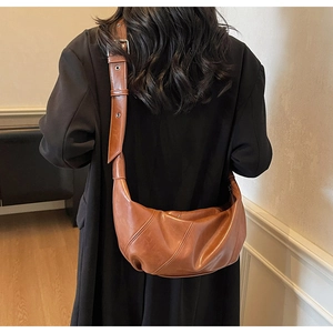 Macro detail of brown leather crescent bag with diagonal textures and adjustable strap