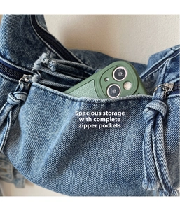 Detail view of denim bag external pocket with zipper and frayed edge showing phone storage