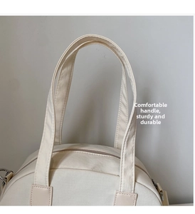 Detail of beige canvas mini shell bag showing durable top handles and zipper closure