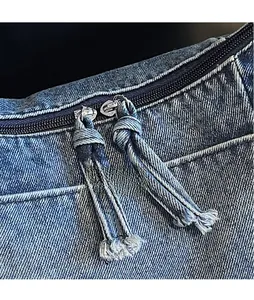 Detail of double-way metal zipper with long denim fringe pullers on a vintage wash bag