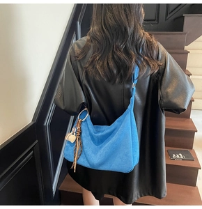 Detail of bright blue hobo bag with suede texture, decorative charm and printed silk scarf