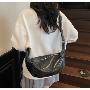 Model wearing a black crescent leather shoulder bag on a staircase in soft daylight