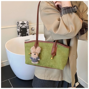 Detail of green suede tote bag with brown leather handles and a plush puppy charm