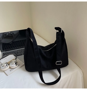 Detail view of a black suede shoulder bag on a desk next to laptop and headphones