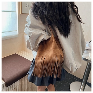 Brown suede bucket bag with long tassels and thin shoulder strap shown in a lifestyle scene