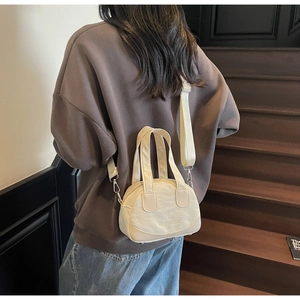 Modern cream shell crossbody bag styled on shoulder in minimalist indoor setting