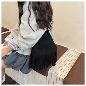 Detail of a black suede hobo bag with long bohemian fringe tassels worn on the shoulder