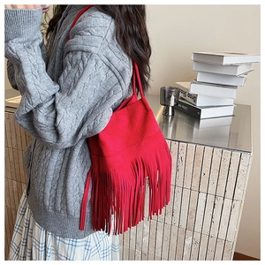 Detalle de bolso tipo cubo rojo con flecos combinado con jersey gris y falda de cuadros