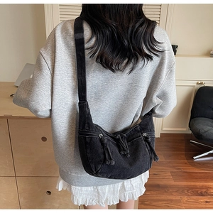 Rear view of model wearing a black denim crossbody bag with dual pockets and tassels
