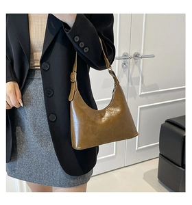 Detail of a brown leather shoulder bag with adjustable strap on a black blazer