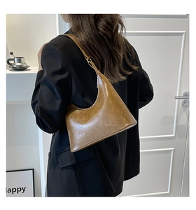 Brown faux leather crescent hobo bag worn on the shoulder in a minimalist indoor setting