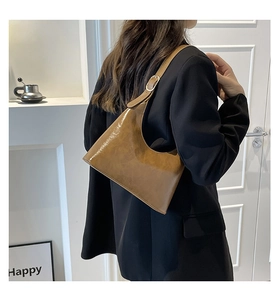 Detailed macro view of the glossy brown leather texture and adjustable strap of the shoulder bag