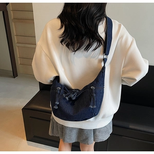 Detail of dark blue denim crescent crossbody bag with tassel zippers on model