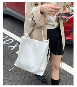 Outdoor commute scene of cream drawstring tote bag paired with khaki trench coat