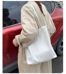 Lifestyle shot of large white leather bucket bag worn with khaki trench coat