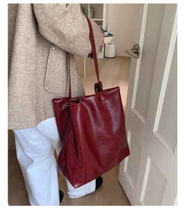 Detail of burgundy glossy leather tote bag worn by model with wide shoulder strap
