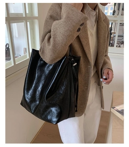 Detail of glossy black tote bag with silver drawstring buckle in a lifestyle setting